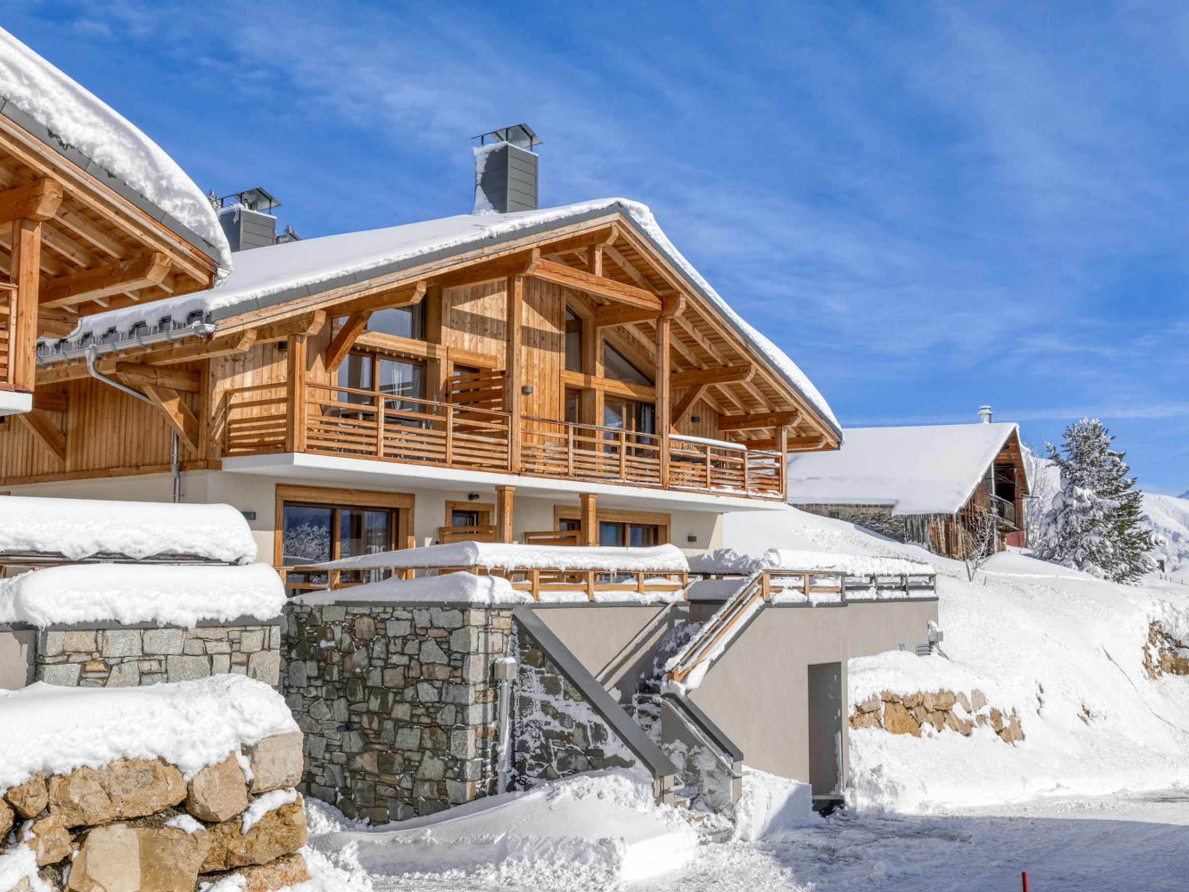 A wooden chalet with a stone foundation, wooden balconies, and a staircase leading to the entrance.