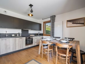 A modern kitchen with dark cabinets, a wooden dining table, and a hanging light fixture.