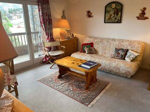 A cozy living room with a sofa, a wooden coffee table, a patterned rug, and a view of a mountain through a sliding door. - Courchevel 1850 Center, 2-Room Apt, 4 People, Wifi, Balcony (Courchevel)
