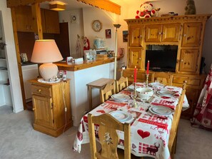 A cozy dining area with a wooden table set for four, a lamp, and a TV in the background. - Courchevel 1850 Center, 2-Room Apt, 4 People, Wifi, Balcony (Courchevel)