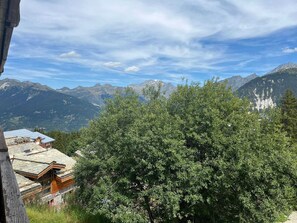 A mountain cabin with a stone roof and wooden walls, surrounded by lush greenery and a view of distant mountains. - Courchevel 1850 Center, 2-Room Apt, 4 People, Wifi, Balcony (Courchevel)