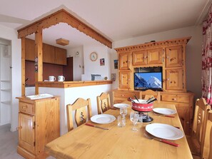 A dining area with wooden furniture, a television, and a kitchen in the background.