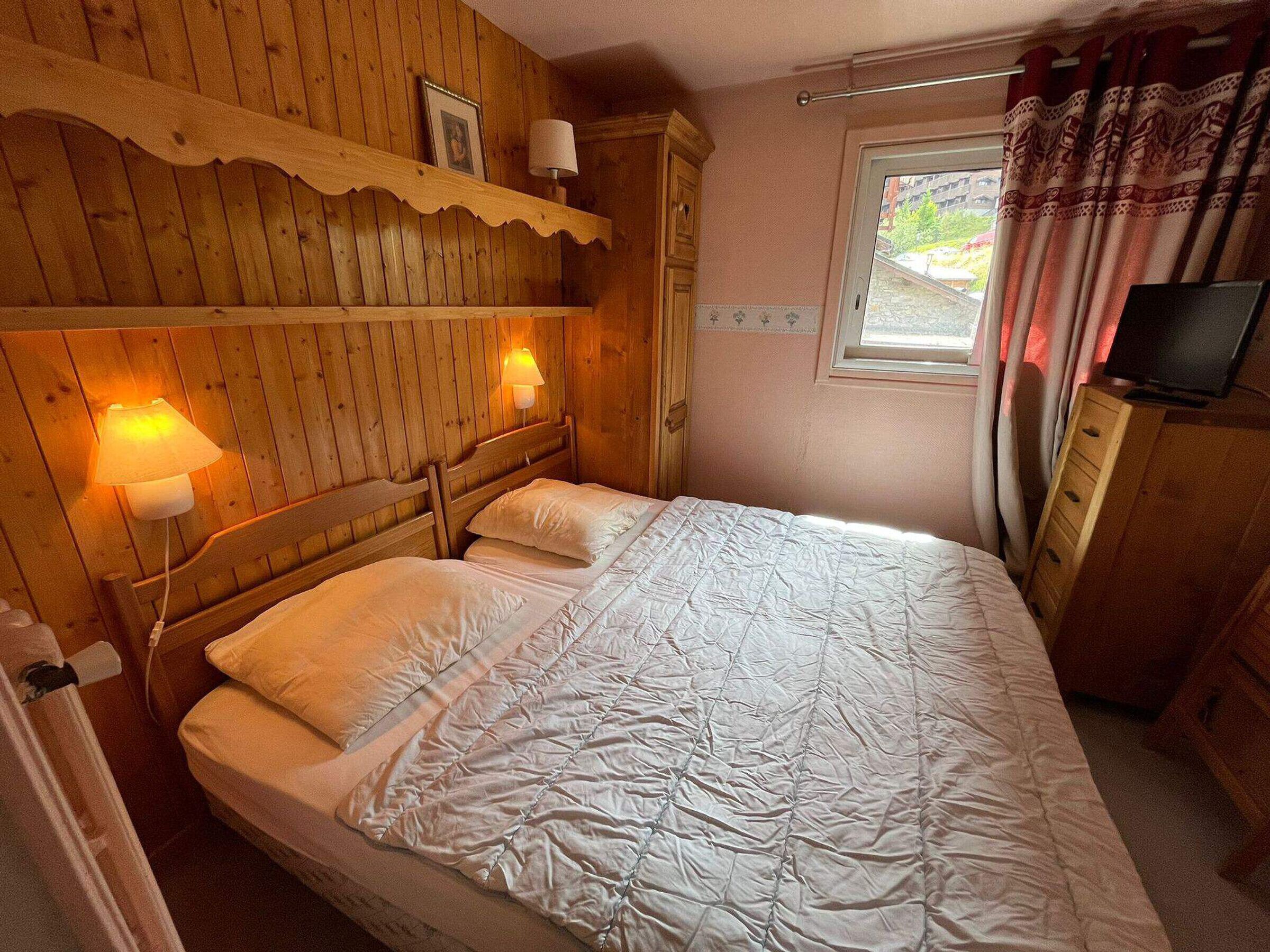 Ein Schlafzimmer mit Holzwänden, einem Bett, zwei Wandleuchten, einem Fernseher und einem Fenster mit Vorhängen.