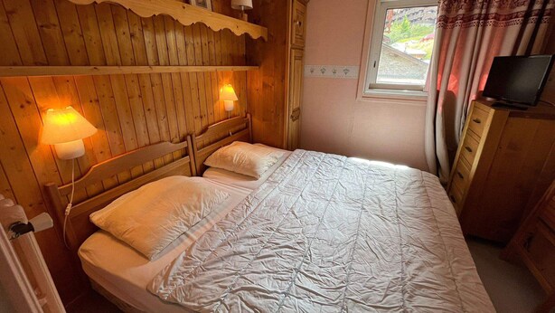 Ett sovrum med träpanel på väggarna, en säng, två vägglampor, en tv och ett fönster med gardiner.