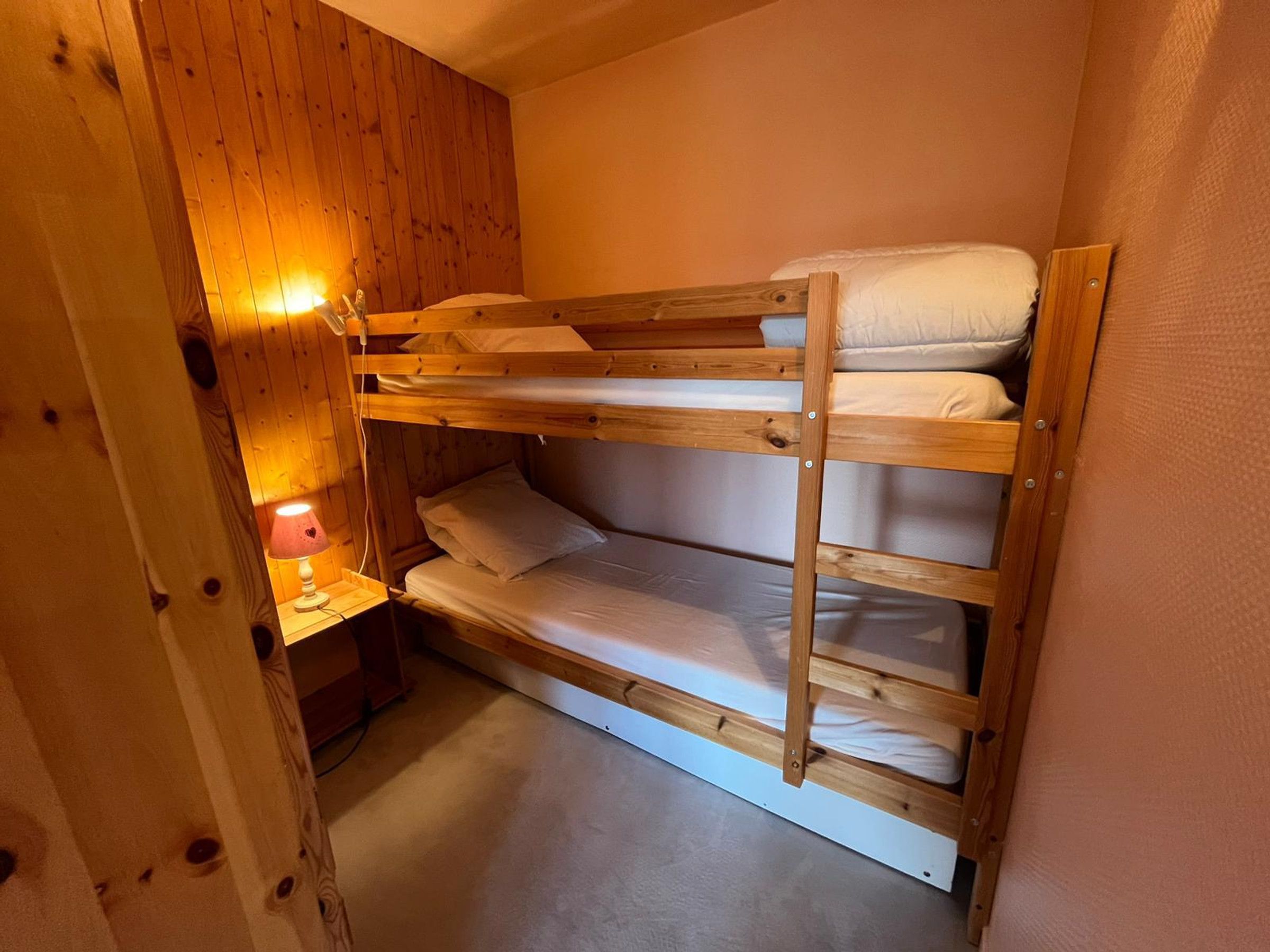 Dormitorio con literas, paredes de madera y una mesita de noche con lámpara.