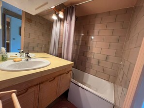 A bathroom with a wooden vanity, a sink, a mirror, a shower curtain, and a bathtub.