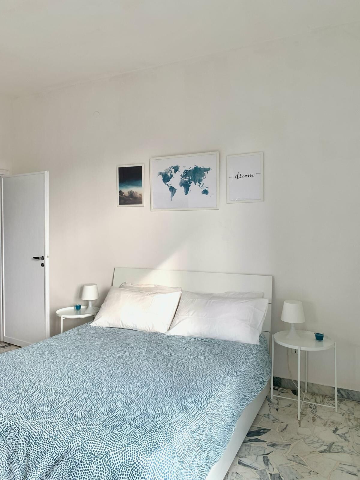 Ein Schlafzimmer mit einem Bett, zwei Nachttischen, einer Tür und drei gerahmten Bildern an der Wand.
