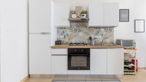 Een compacte keuken met witte kastjes, een zwarte oven, een roestvrijstalen spoelbak en een betegelde spatwand.