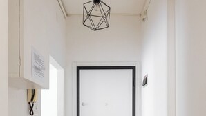 Een hal met een witte deur, een hangende geometrisch lichtarmatuur en een bank.