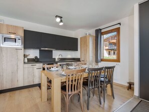 A modern kitchen with dark cabinets, a wooden dining table set for four, and a large window offering a view of a building outside.