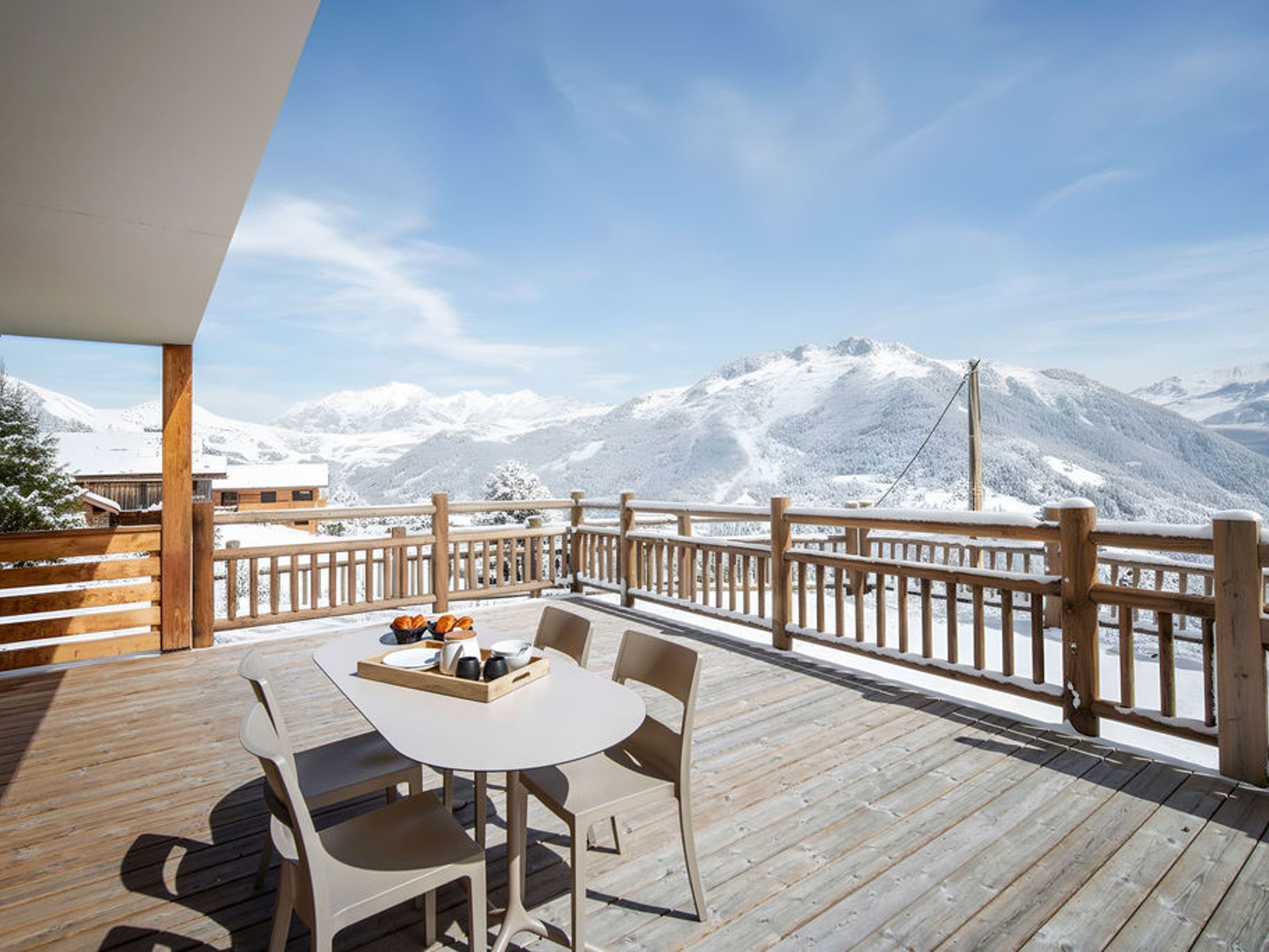 Terraza de madera con mesa y sillas, con vistas a un paisaje nevado de montañas.