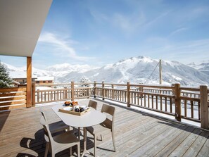 A wooden deck with a table and chairs, overlooking a snowy mountain landscape. - 3-Bedroom Apt in Les Saisies, 8 ppl, near slopes (Les Saisies)