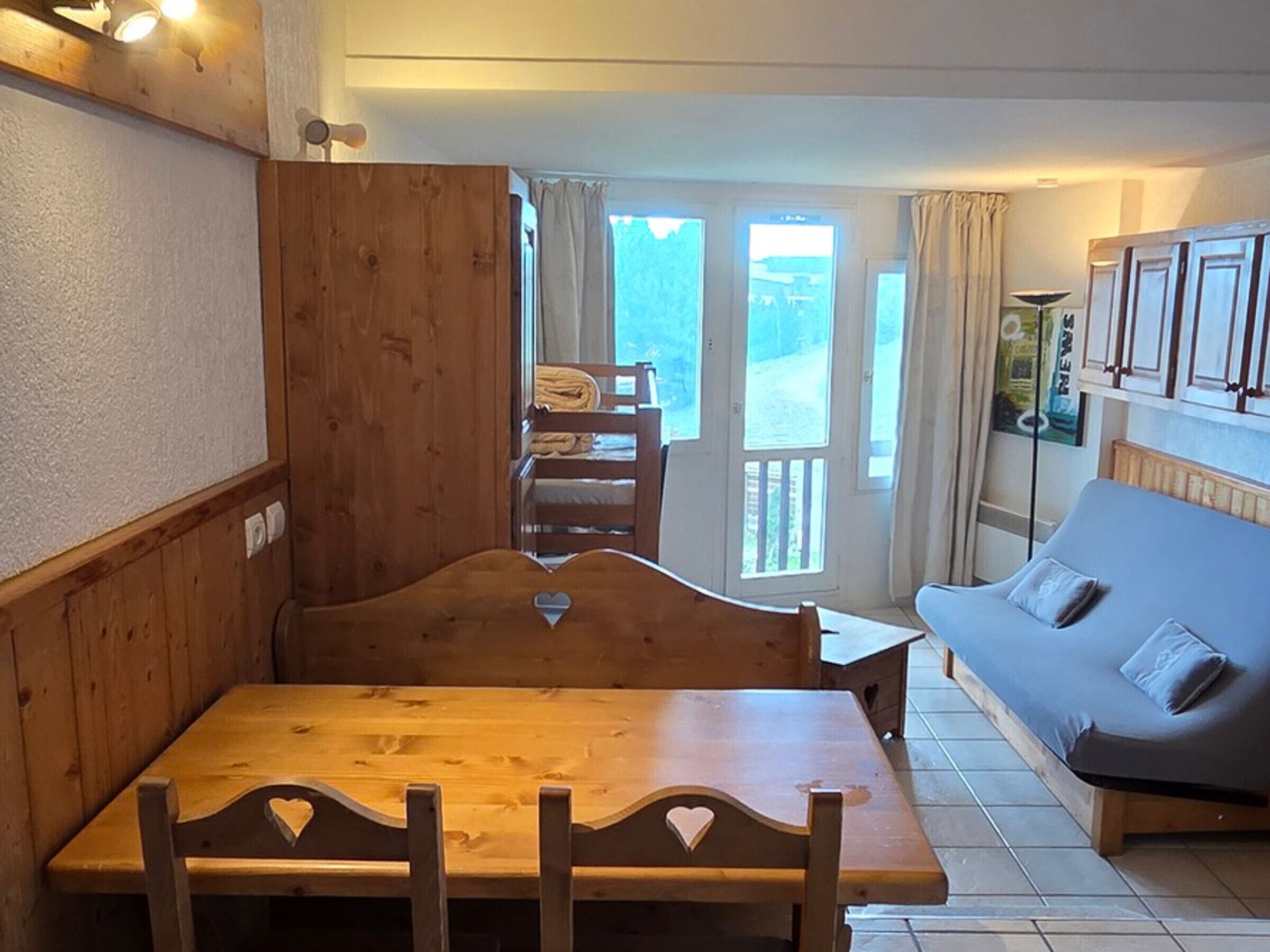 A cozy room with a wooden dining table and benches, a sofa, and a view of the outdoors through a glass door.