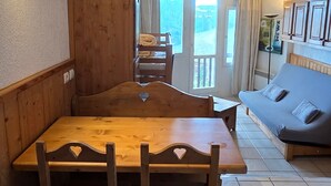 Ein gemütliches Zimmer mit einem Holzesstisch und Bänken, einer Couch und Blick ins Freie durch eine Glastür.