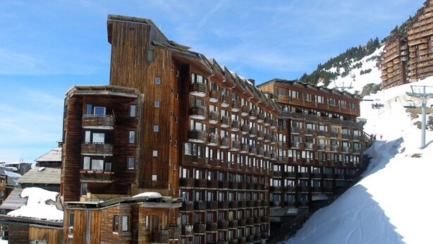 Ein großes Holzhotel mit mehreren Balkonen und einer Skipiste im Hintergrund.