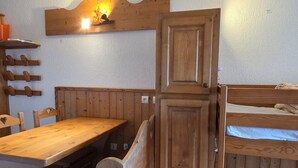 Ein Zimmer mit einem Holztisch, Stühlen, einem Etagenbett und einem an der Wand befestigten Regal mit einer Leuchte.