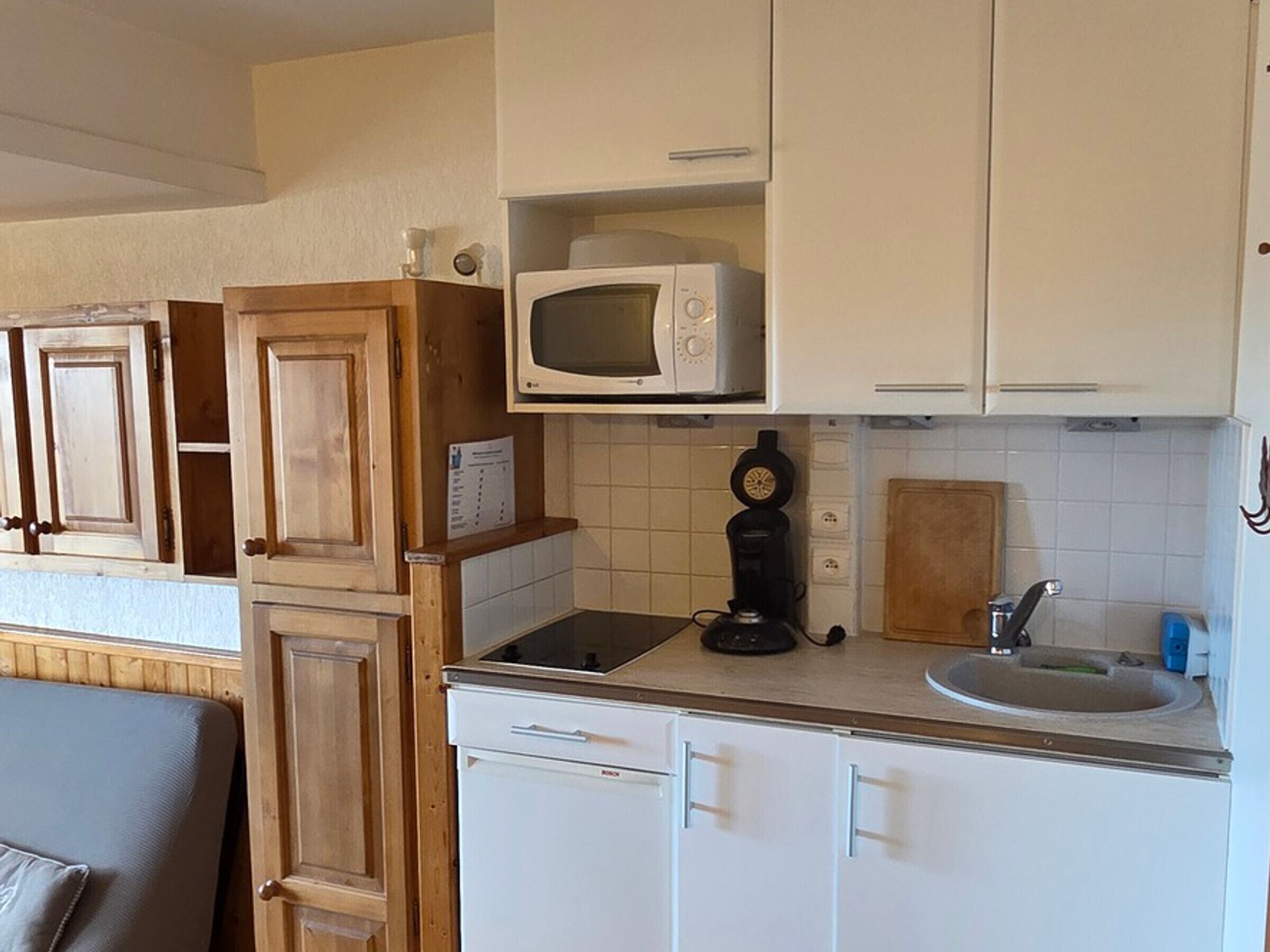 A compact kitchen with white cabinets, a microwave, a coffee maker, and a sink.
