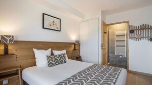A bedroom with a wooden headboard, a bed with patterned bedding, a nightstand with a lamp, a framed picture on the wall, and a door leading to a bathroom. - Comfortable T2 cabin for 6, ski shuttle, parking included (Les Saisies)