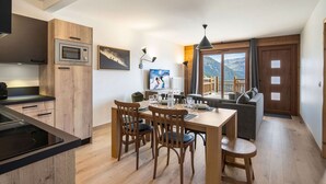 A modern kitchen with wooden cabinets, a built-in oven, and a dining area with a wooden table and chairs. - Comfortable T2 cabin for 6, ski shuttle, parking included (Les Saisies)