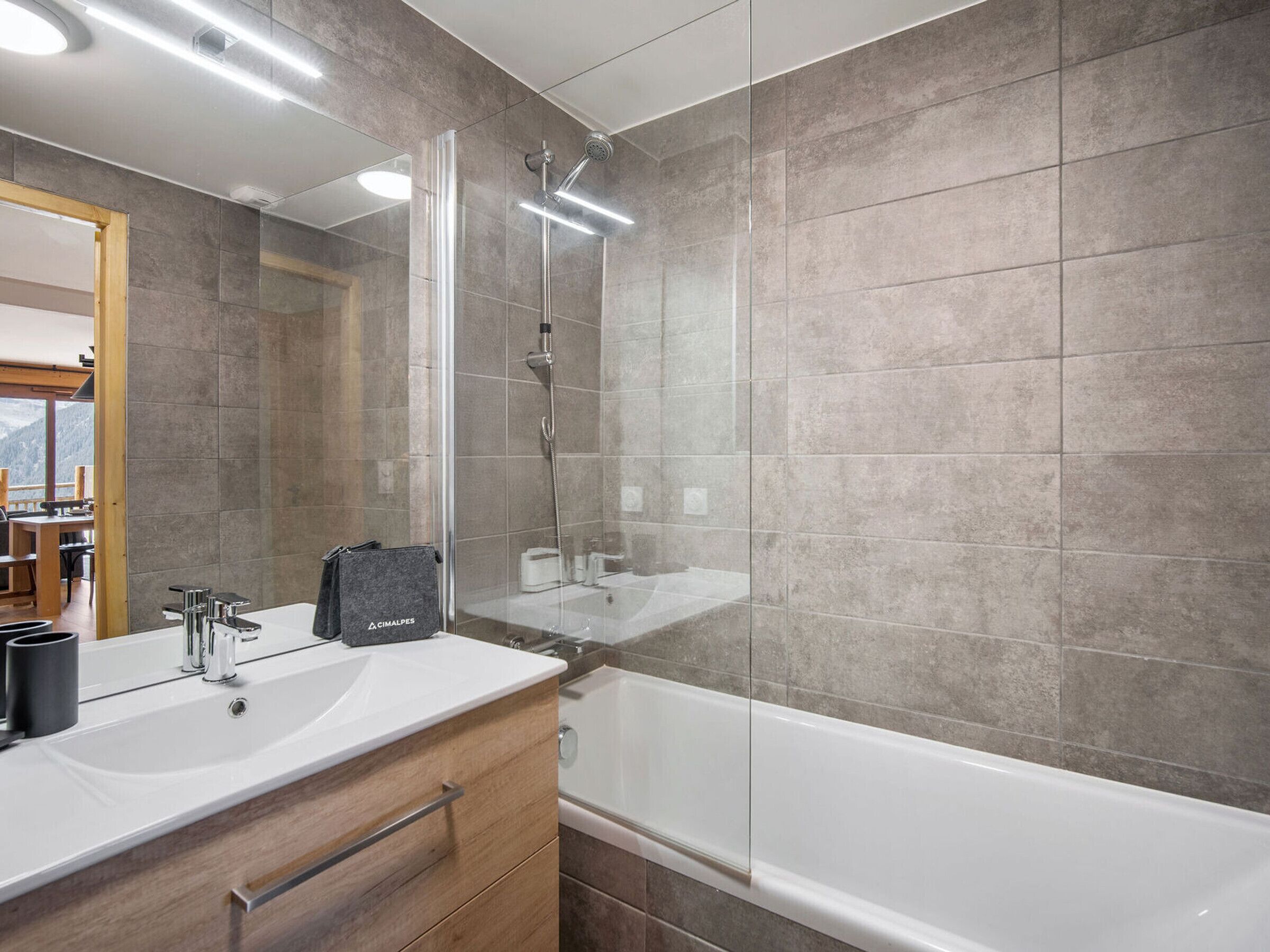 A modern bathroom with a glass-enclosed shower, a white sink, and a wooden vanity.