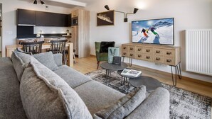 A modern living room with a grey sofa, a dining area with a wooden table, and a kitchen with dark cabinets. - Comfortable T2 cabin for 6, ski shuttle, parking included (Les Saisies)