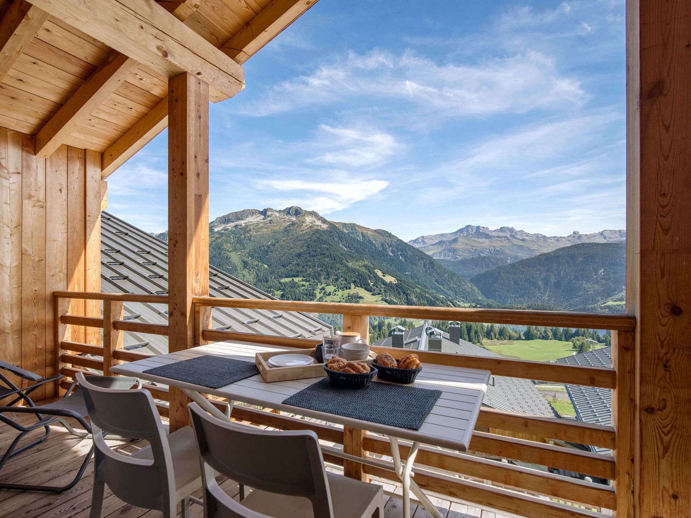 Een houten terras met een ontbijttafel, met uitzicht op een bergachtig landschap.