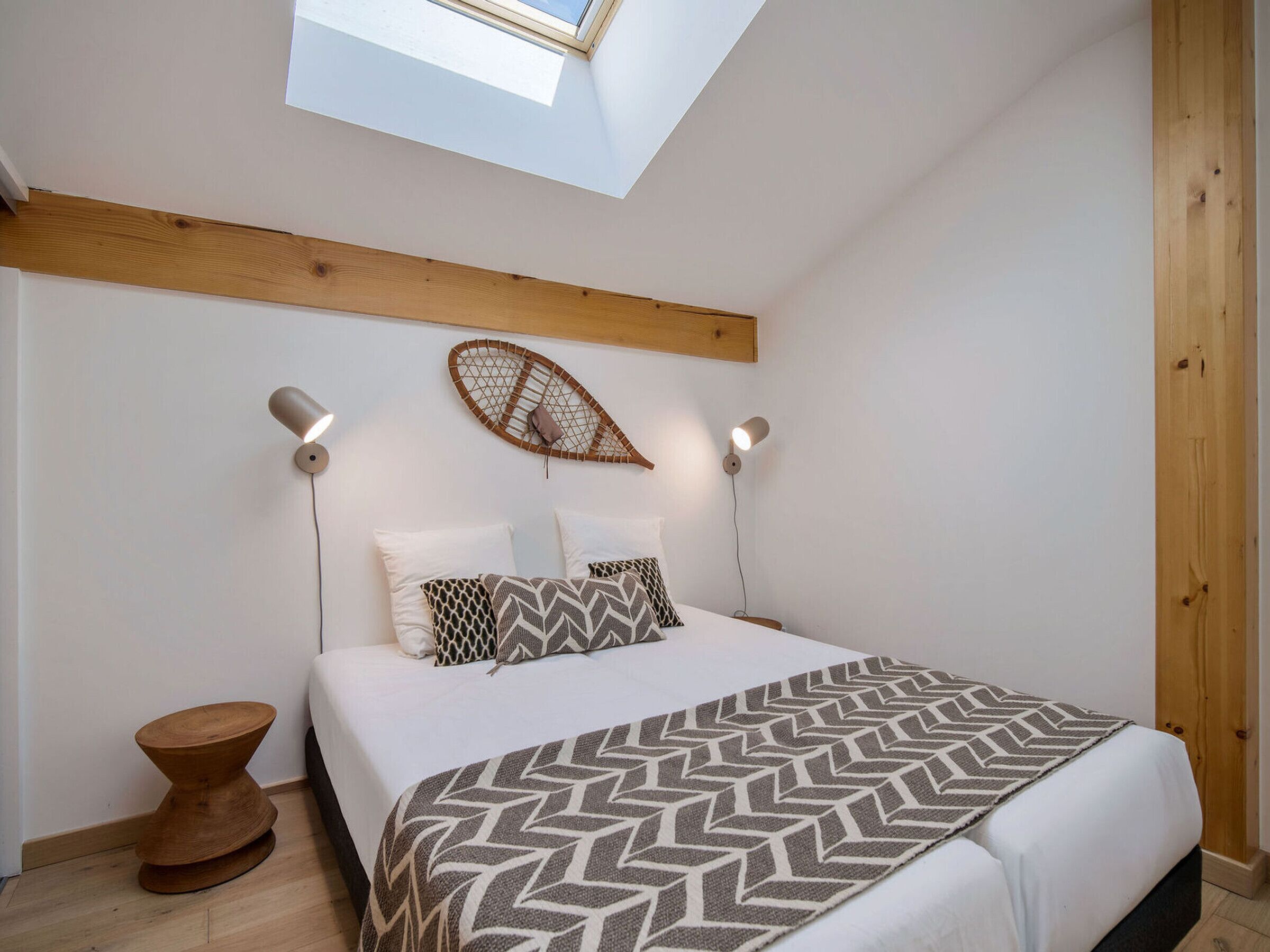 Un dormitorio con tragaluz, cama con ropa de cama estampada, dos lámparas de noche y cabecera de madera.