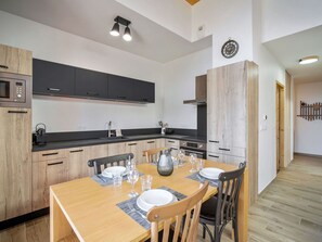 A modern kitchen with dark cabinets, a wooden dining table set for four, and a visible microwave. - Comfortable T3 Apartment in Les Saisies with Balcony and Parking (Les Saisies)