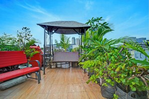 A rooftop terrace with a red bench, a covered seating area, and potted plants. - OYO 94764 Syariah KamarGue (Jakarta)
