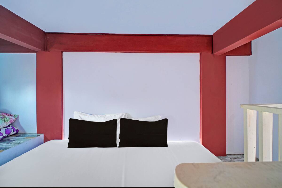 A room with a bed, pillows, a small table, and a railing.