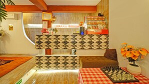 Camera d'albergo con tavolo a scacchi, una scacchiera, un divano, un tavolino con un vaso di fiori e un'area reception con un cartello 'Happy Birthday'.