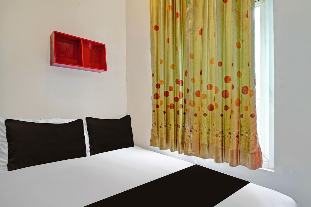 A bedroom with a bed, two black pillows, a red shelf, and a window with polka dot curtains.