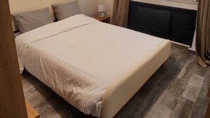 A bedroom with a bed, a nightstand, a lamp, a window with blinds, and a wooden floor. - 70m2 apartment in Dijon, 4th floor without elevator, 5 minutes from Zenith (Dijon)
