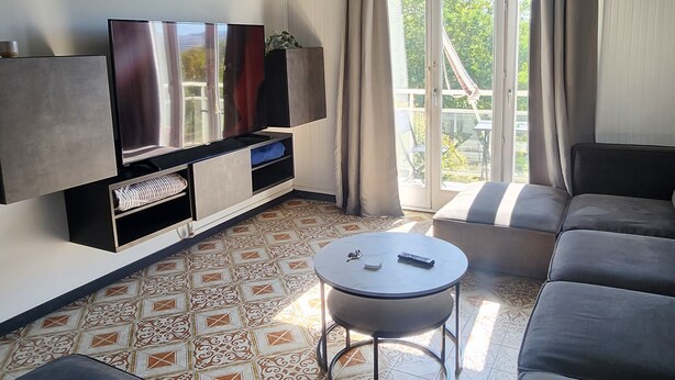 A modern living room with a flat-screen TV, a sofa set, a coffee table, and a patterned floor. - 70m2 apartment in Dijon, 4th floor without elevator, 5 minutes from Zenith (Dijon)