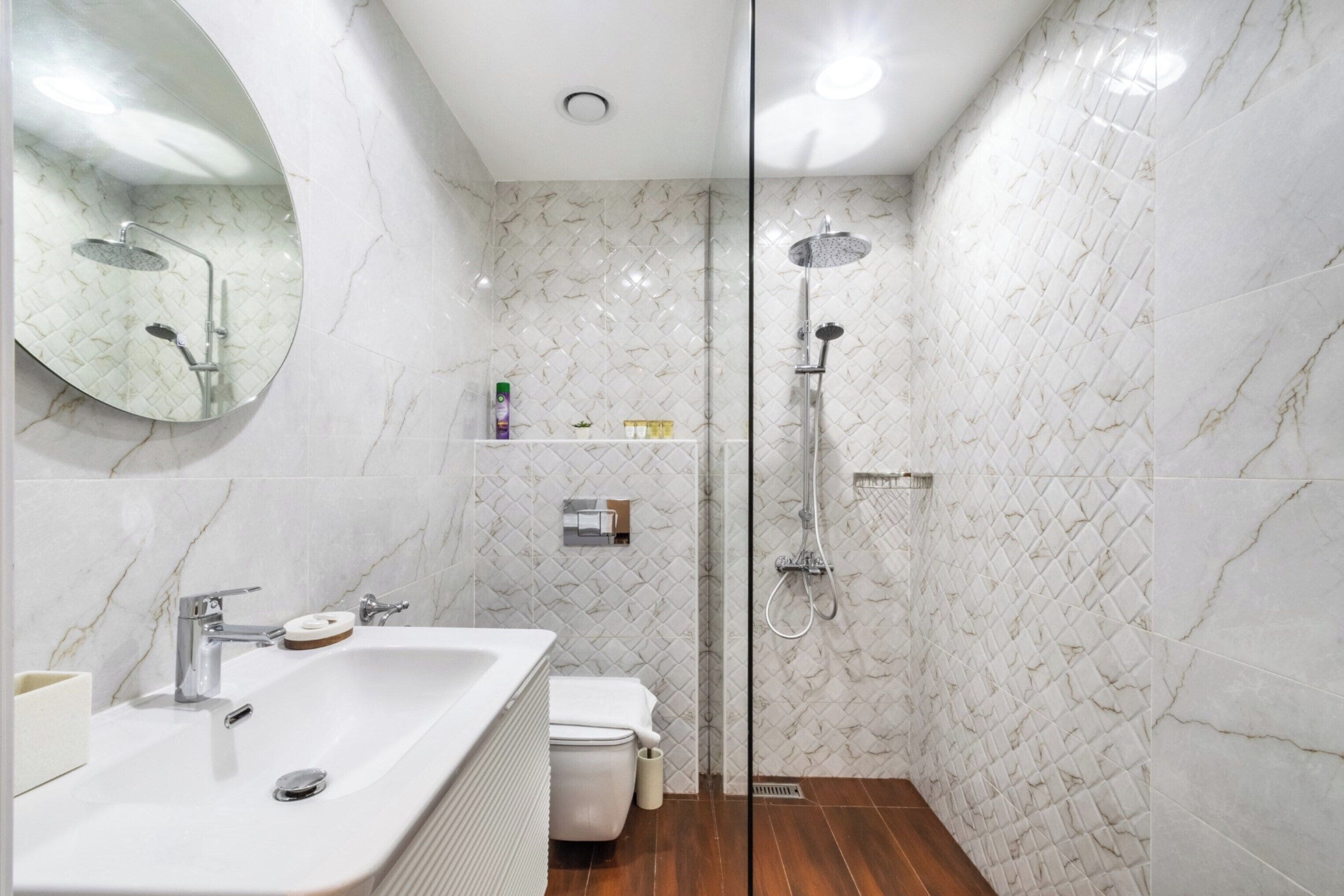Un bany modern amb un lavabo de marbre blanc, un vàter i una dutxa amb aixeta de mà.