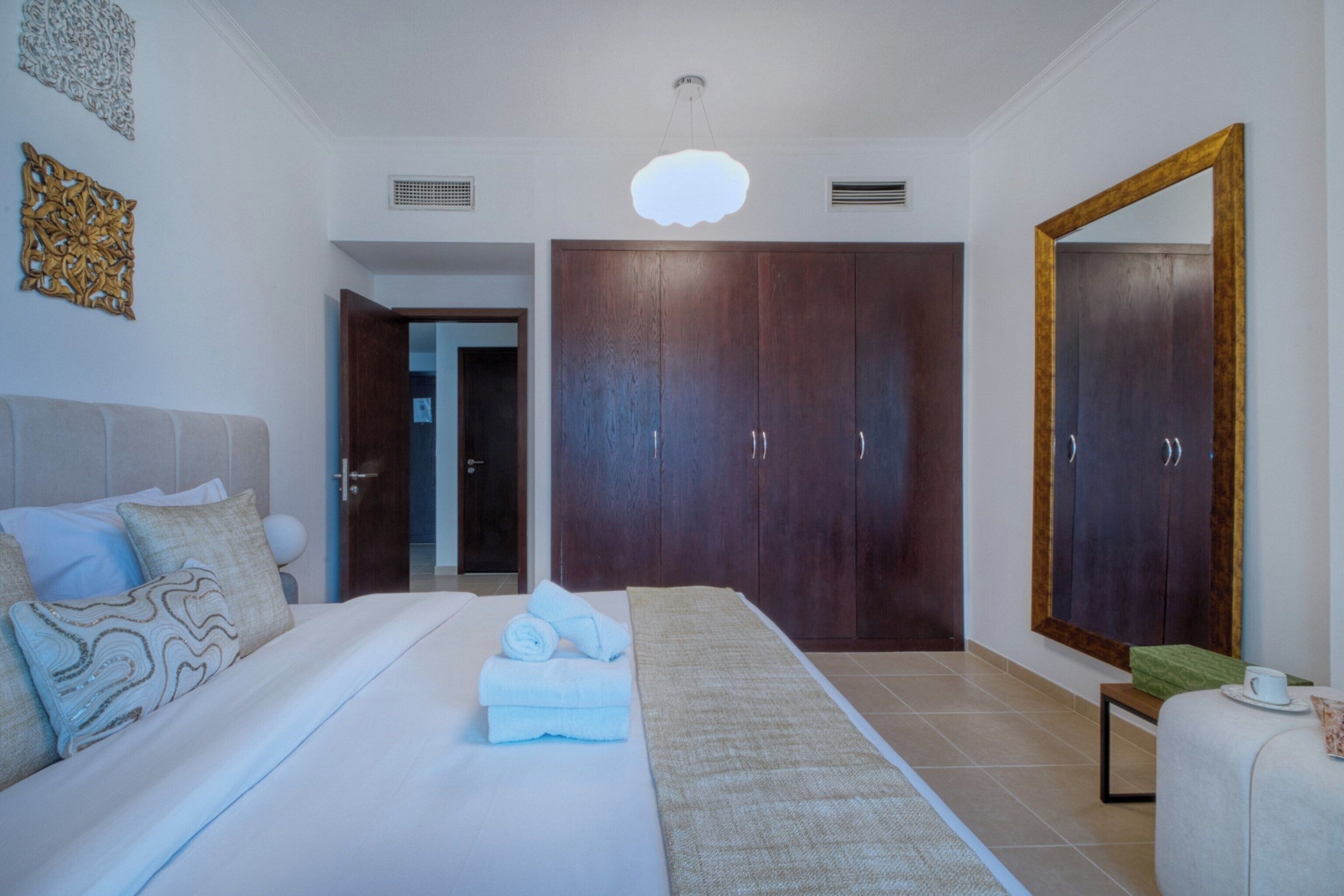 Ein Hotelzimmer mit einem Bett, einem großen Spiegel, einem Kleiderschrank und einer Tür zu einem weiteren Raum.