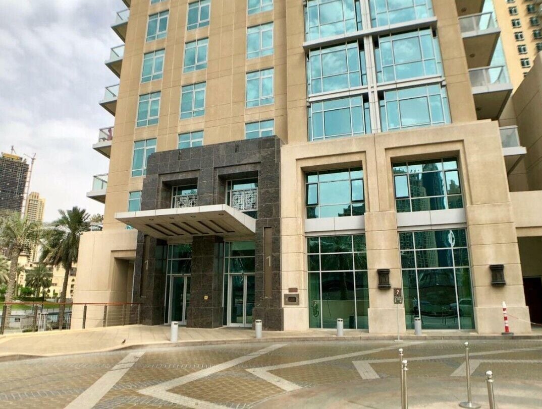 Un bâtiment moderne doté d’une façade en verre, d’un hall d’entrée couvert et d’une place dallée devant l’entrée.