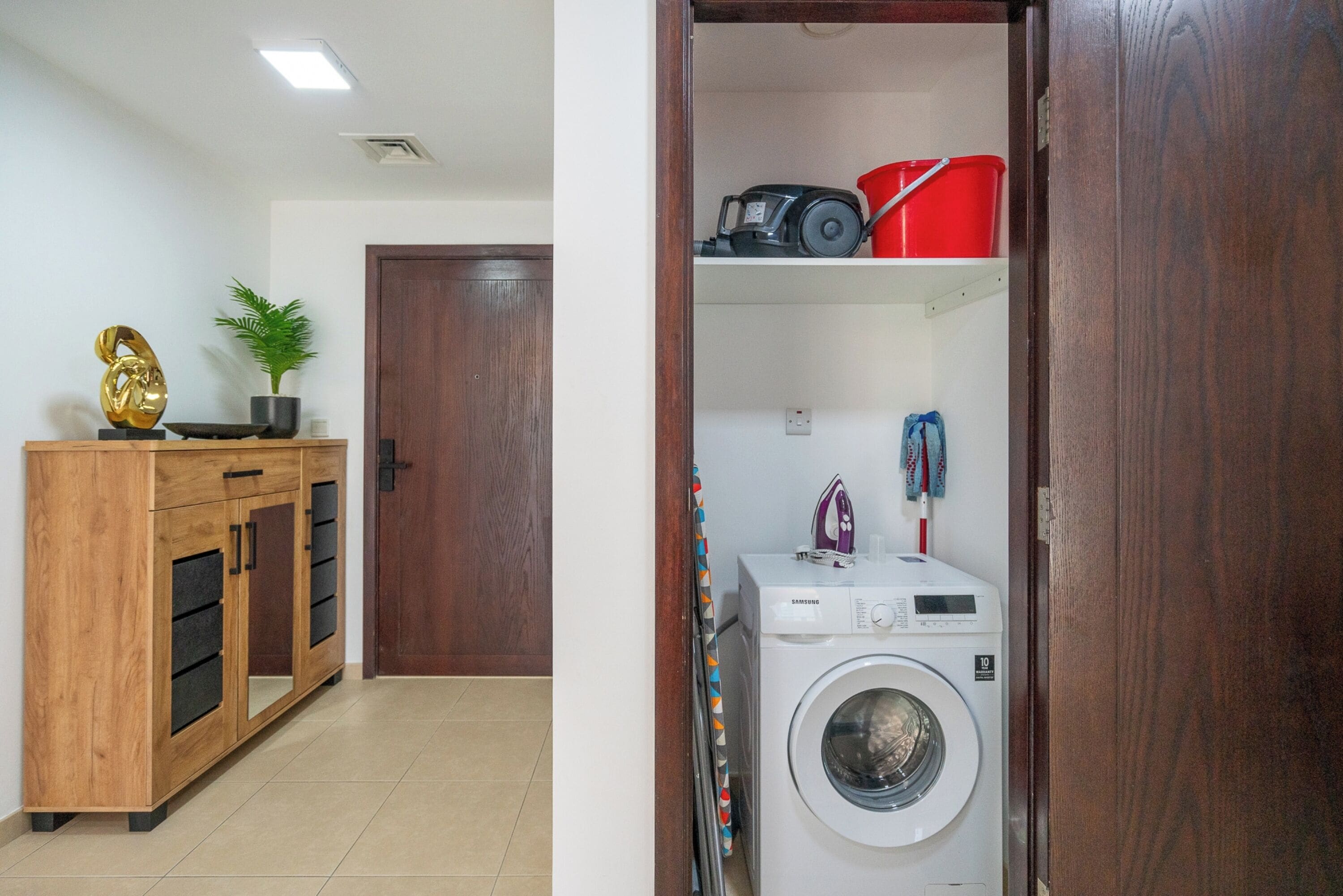 A laundry area with a washing machine, a wooden cabinet, and a potted plant.
