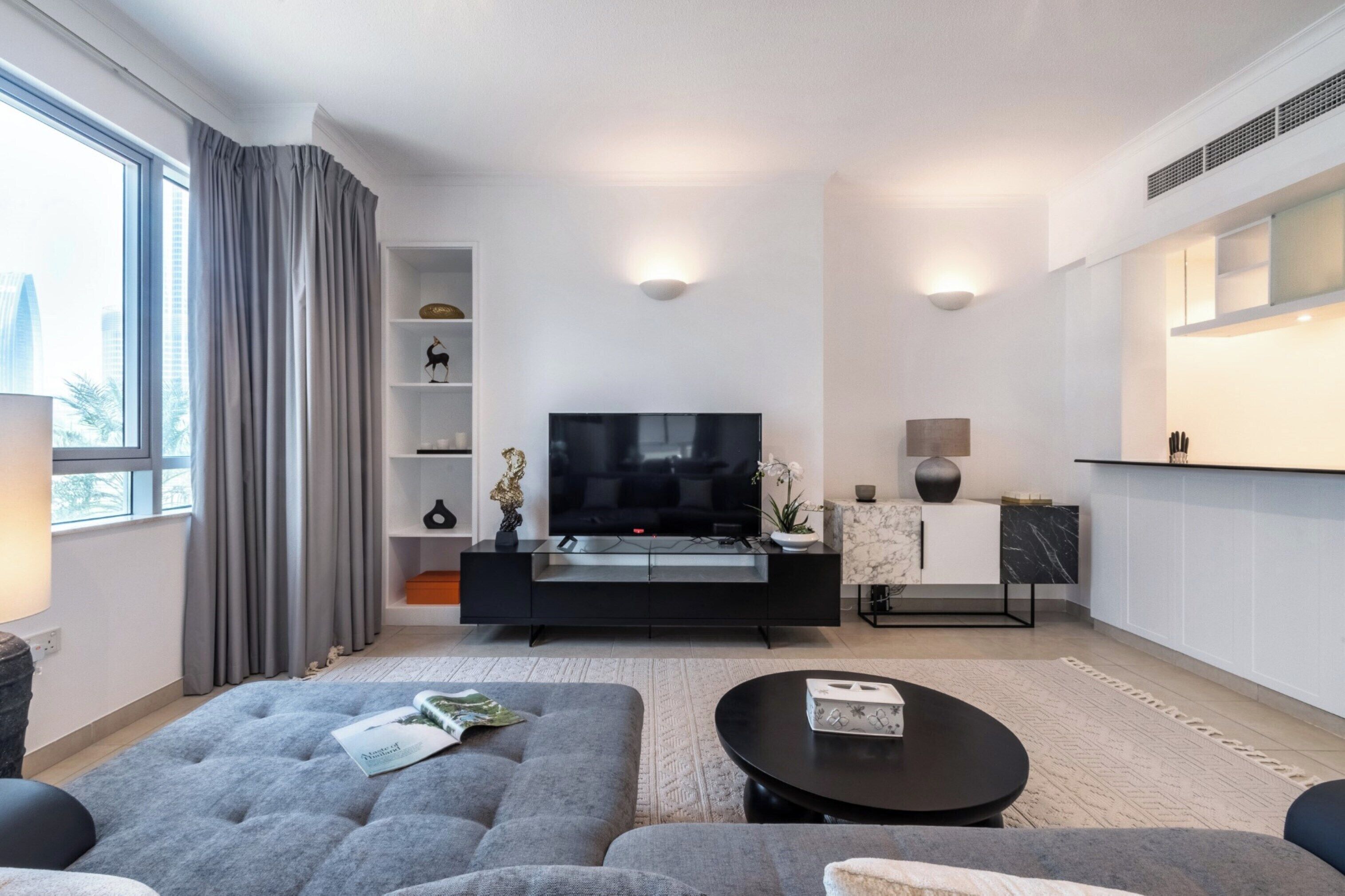 Un salon moderne avec un grand téléviseur à écran plat, un canapé gris et une table basse.