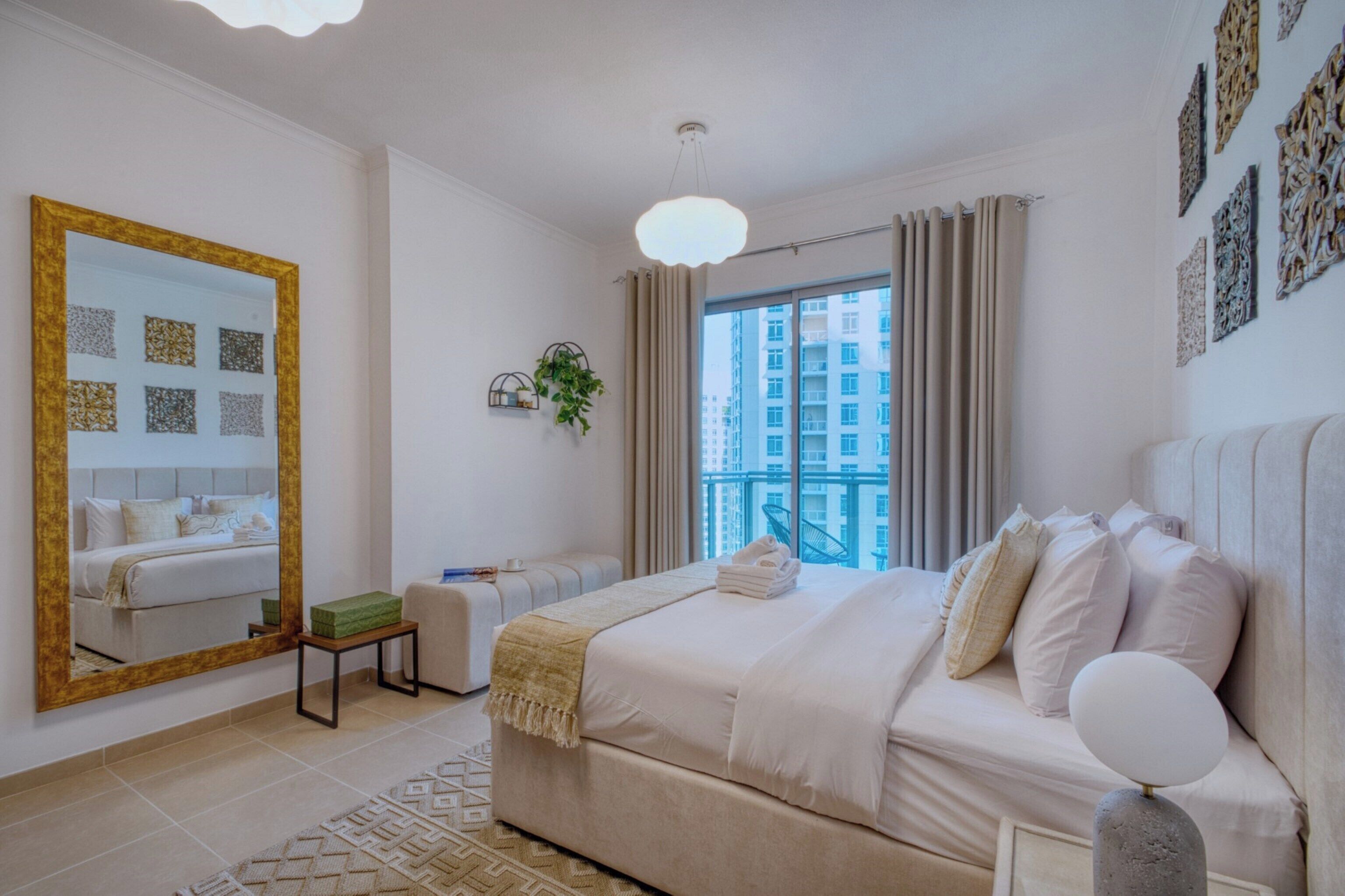 Une chambre à coucher avec un grand lit, une table de chevet, un miroir et une vue sur le paysage urbain par la fenêtre.