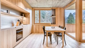 Een moderne keuken met houten kastjes, een groot raam en een eethoek met tafel en stoelen.