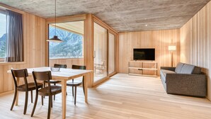 Een modern interieur met een houten eettafel, stoelen, een bank, een televisie en een groot raam met uitzicht op bergen.
