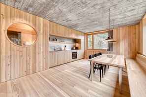 A modern kitchen with wooden walls, a round window, and a dining area with a table and chairs.