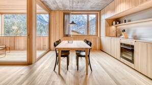 A modern kitchen with wooden cabinets, a dining table, and a view of mountains through large windows. - Appartmentshaus Studa 29 - Studa 7 (Brand)