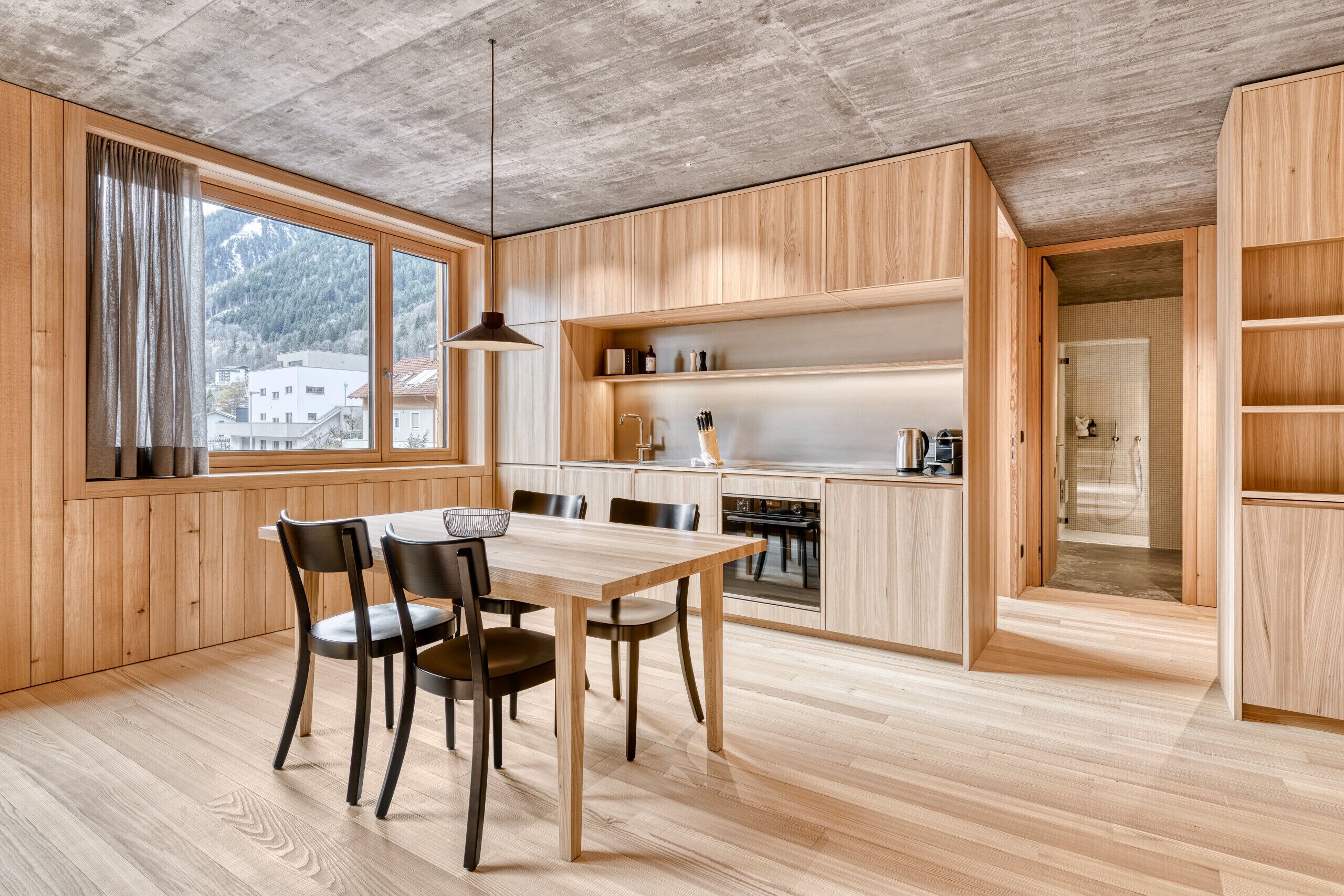 Eine moderne Küche mit Holzschnitzereien, einem Esstisch mit Stühlen und Bergblick durch große Fenster.