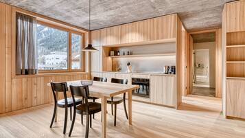 Eine moderne Küche mit Holzschnitzereien, einem Esstisch mit Stühlen und Bergblick durch große Fenster.