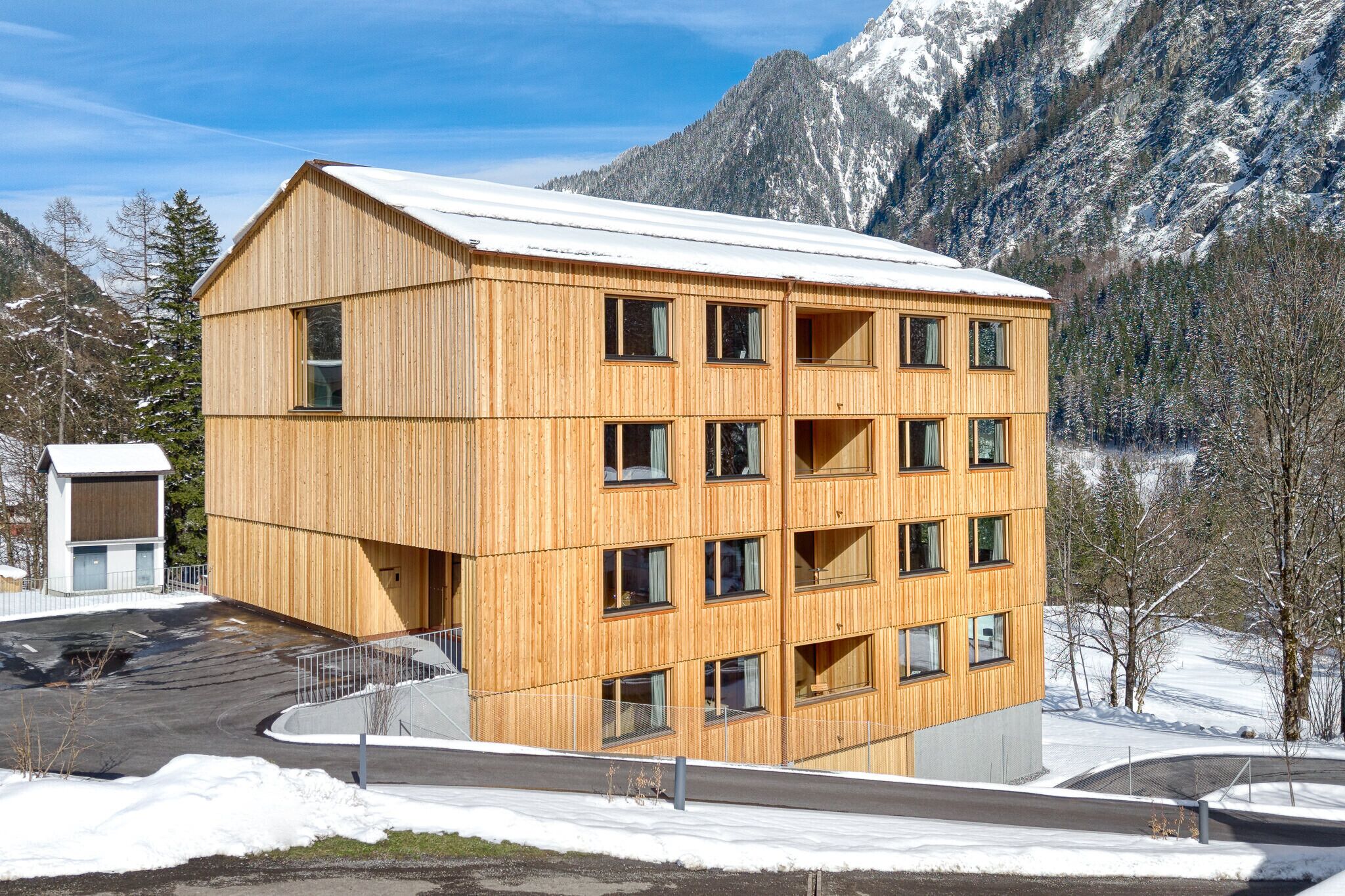 Un edificio de madera de varios pisos con techo inclinado, rodeado de montañas cubiertas de nieve.