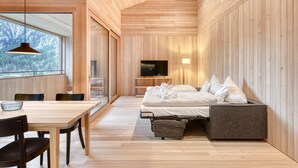 A modern room with a wooden ceiling, a bed with pillows, a TV, and a dining area with chairs and a table.