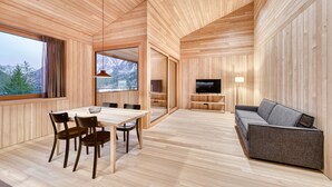 A modern interior with wooden panel walls, a dining area with a table and chairs, a gray sofa, and a TV.