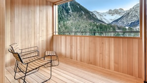 A wooden deck with a bench and a large window overlooking a mountainous landscape.